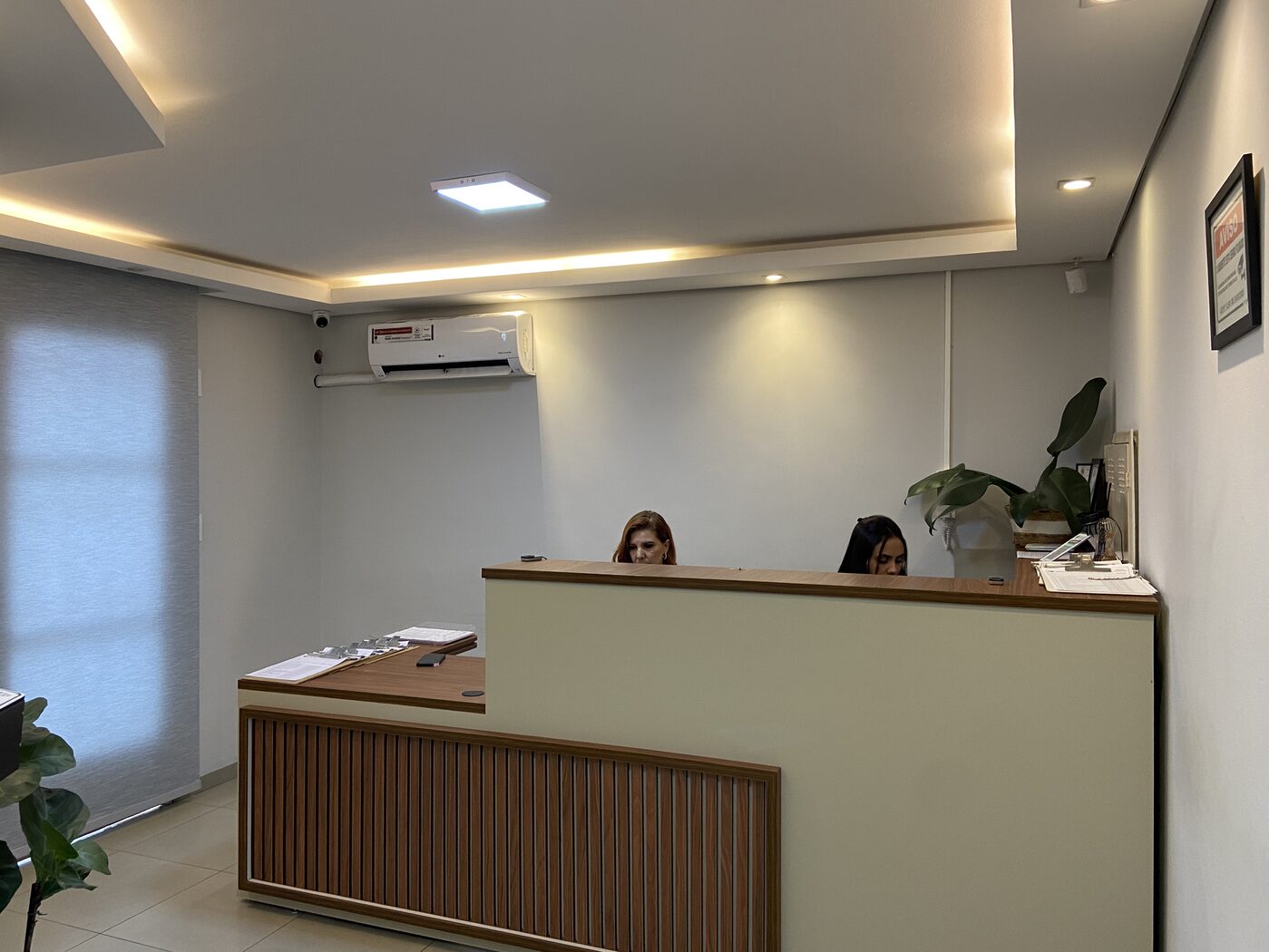 Recepcionista da Atual Medicina atendendo um paciente no balcão da recepção